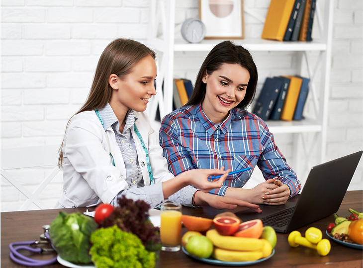 A smiling nutritionist advises a young patient woman on proper nutrition and dieting